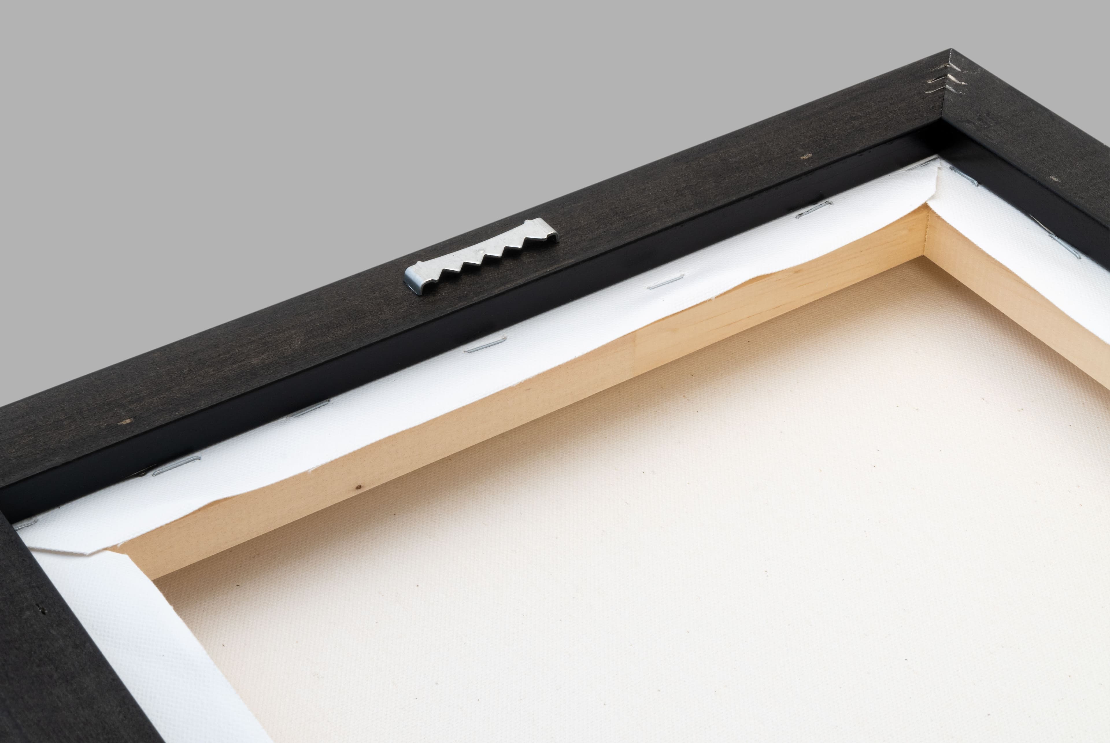 Back of a black floating frame with stretched canvas, wooden bars, staples, and a sawtooth hanger